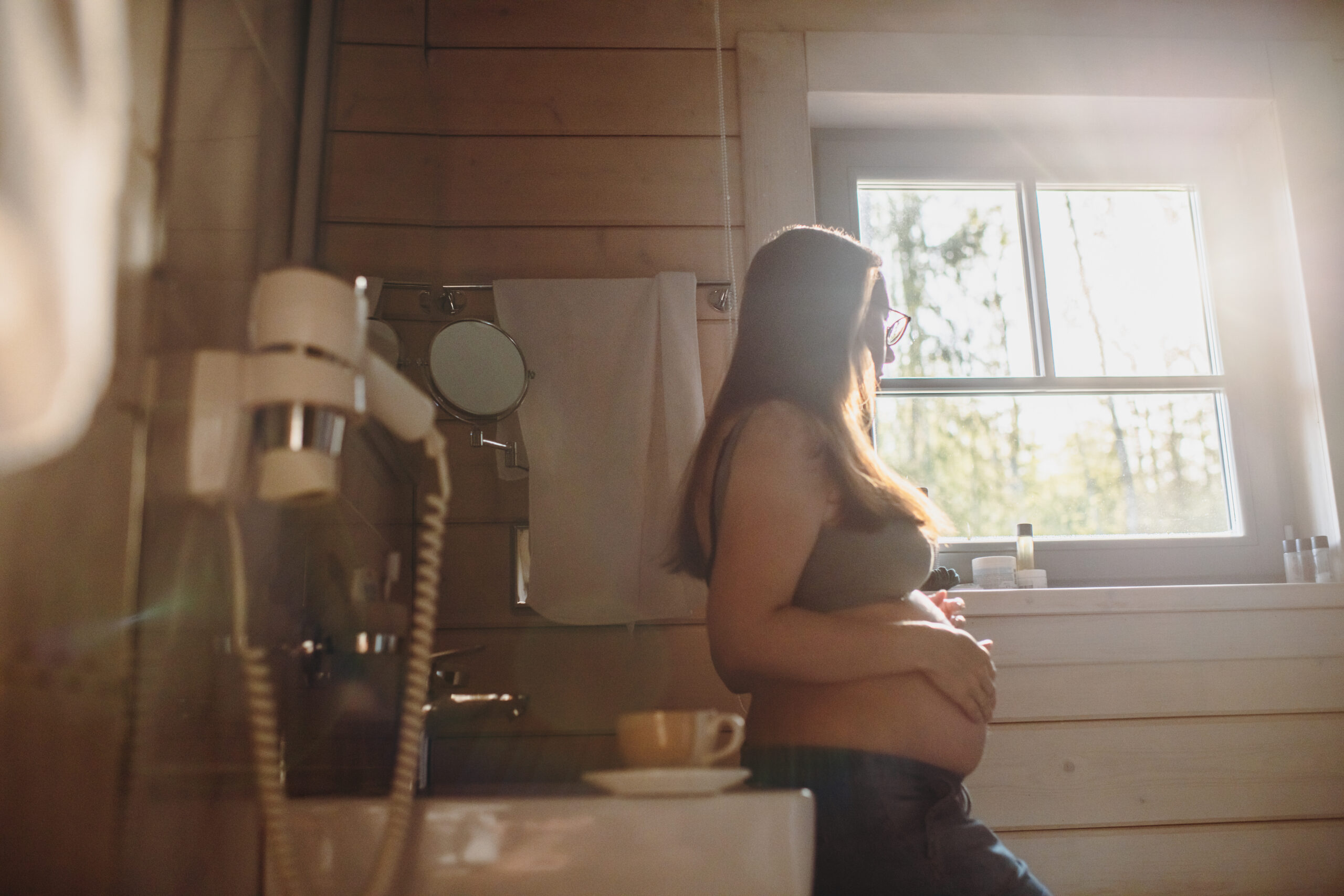 <p>Pregnant woman looking through window in the morning</p>
