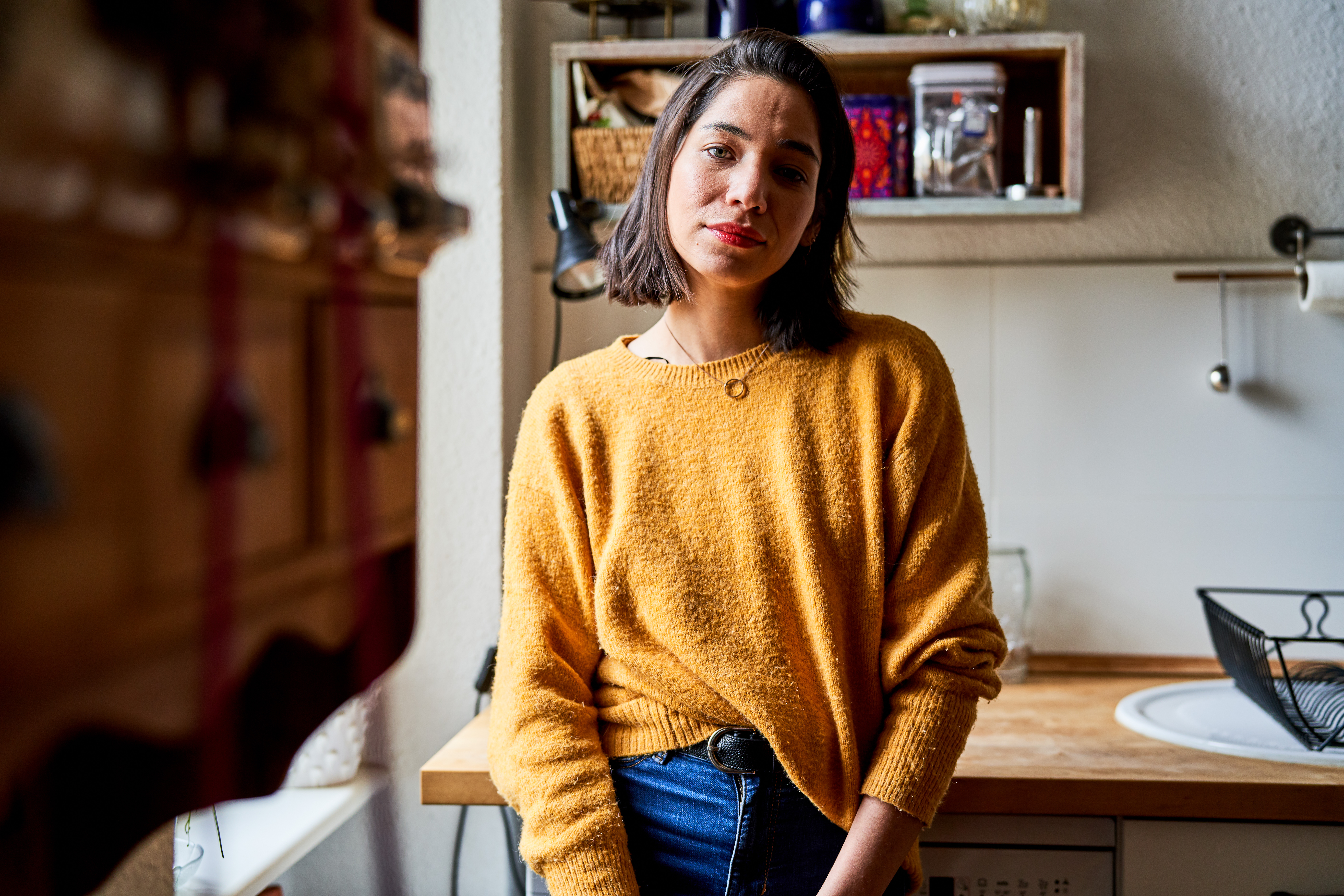 <p>Portrait of a female standing in the kitchen. Woman in casuals leaning to the kitchen counter and staring at camera.</p>